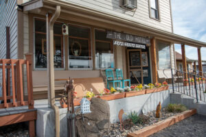 The front porch of the Old Hotel is white with tan beams along the edge. There are flowers in the garden in front of the porch.