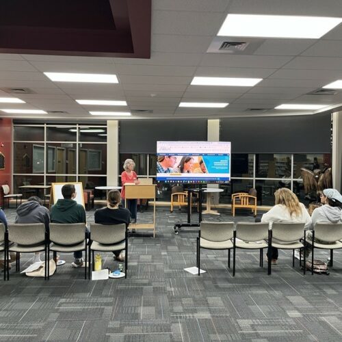 A woman presents a slideshow about college to a group of high school students at a public library.