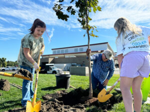 Elena Woodford and Alexis Nicholson help plant one of seven trees at Tapteal Elementary School. (Credit: Courtney Flatt / NWPB)