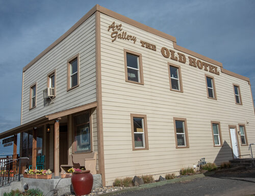 A white two-story building with wood siding. It has a front porch. The sky is blue in the background.